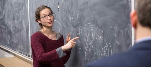 A lady is writing on a chalk board as she is teaching at Imperial College London - Physics